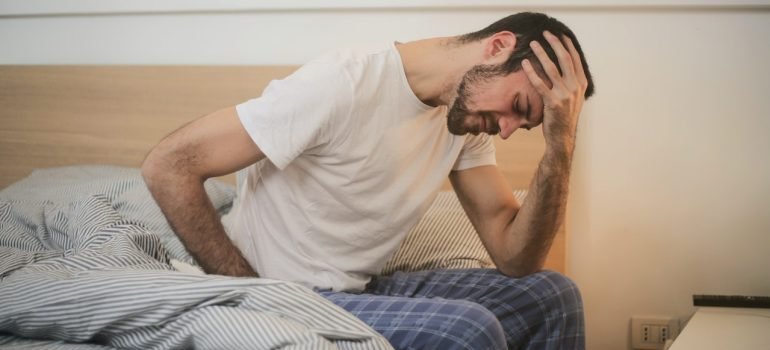 Osoba koja se drži za glavu od umora dok sedi na krevetu