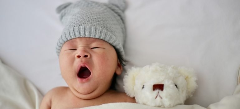 Beba koja leži u krevetu pored plišane igračke i zeva