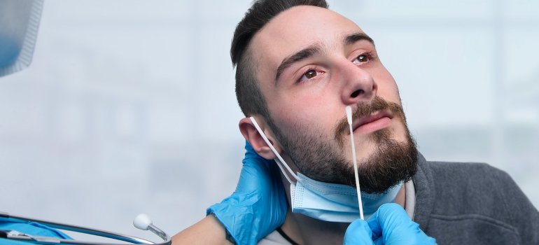 Muškarac sedi dok mu laboratorijski tehničar uzima bris iz nosa.