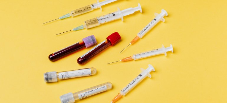 Dve epruvete sa krvlju oko kojih se nalaze špricevi.