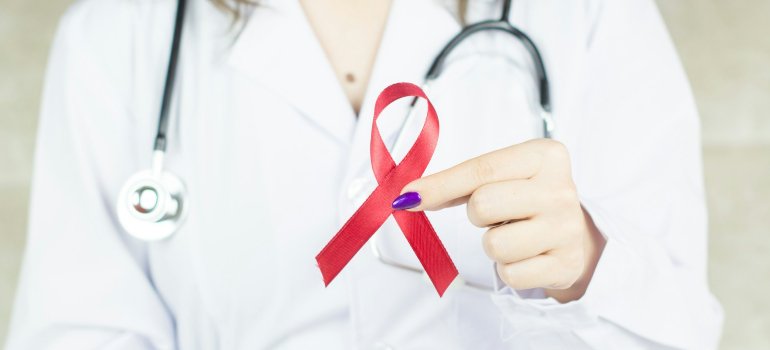 Женщина-врач держит красную ленту — международный символ солидарности с людьми, живущими с ВИЧ