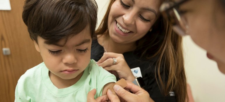 Majka bodri dečaka koji je primio vakcinu dok mu lekar lepi flaster na mesto uboda