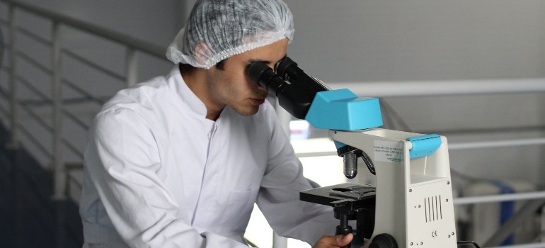 A man in a laboratory is intently looking through a microscope, conducting test panels