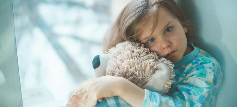 Девочка крепко обнимает своего плюшевого мишку, пытаясь успокоиться. Она слышала, что забор крови у детей может быть неприятным, и ей страшно