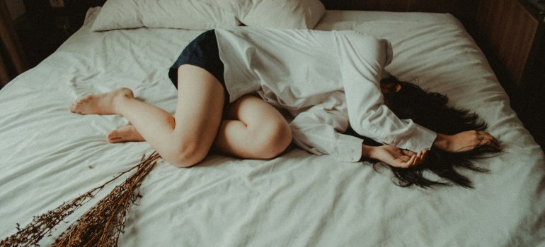 A woman is lying on the bed because of stomach pain due to heavy bleeding accompanied by blood clots during menstruation.