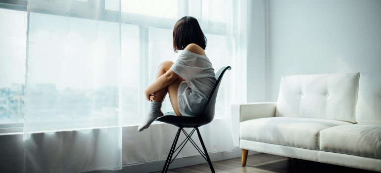 A depressed girl sits on a chair and looks out the window.