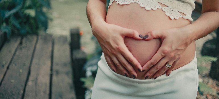 A pregnant woman holding her hands on her belly in the shape of a heart.