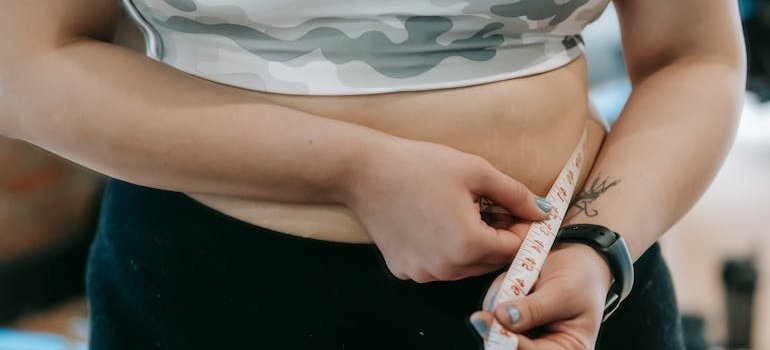 женщина измеряет талию сантиметром и задаётся вопросом, почему набирает вес, даже если ест мало