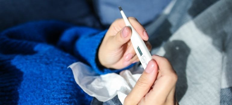 Человек в синем свитере держит термометр