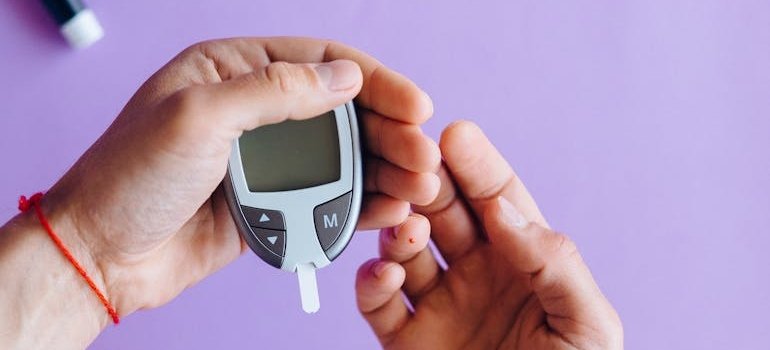 Человек держит глюкометр и тест полоску, готовясь проверить уровень сахара в крови.